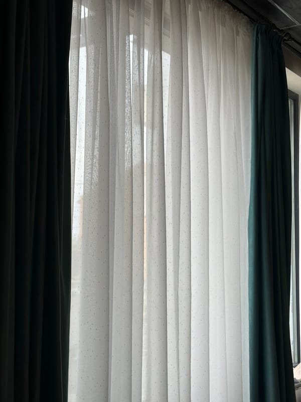 Window with white blinds and green curtains in Sofia