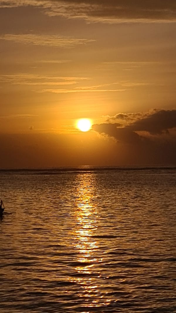 Golden hour over Sanur Beach, boats anchored on calm water.