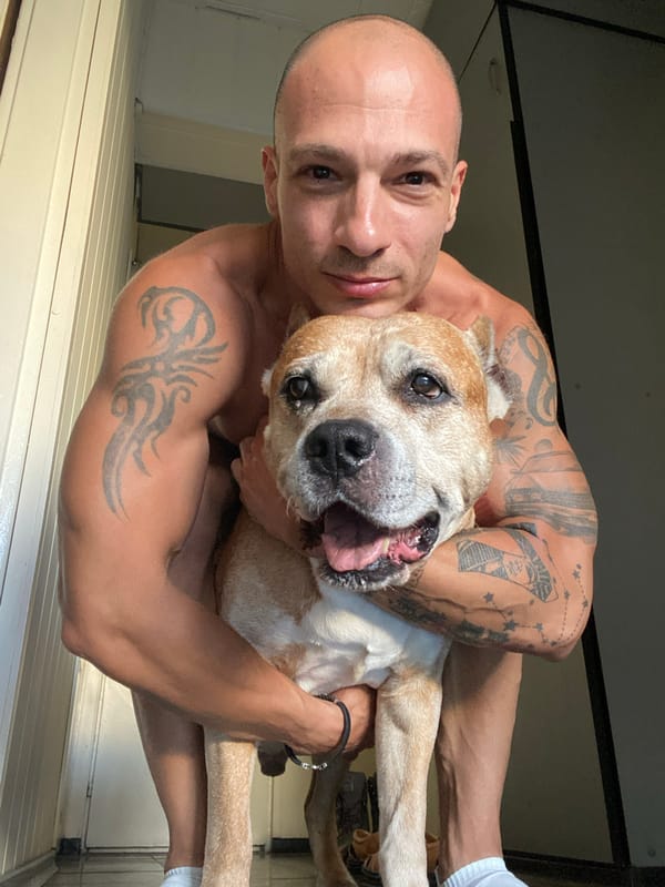 Tattooed person and panting dog share a close indoor moment