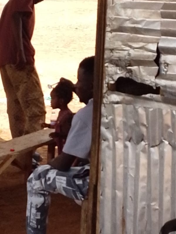 Three people gather near wooden structure in Yaguyili, Ghana