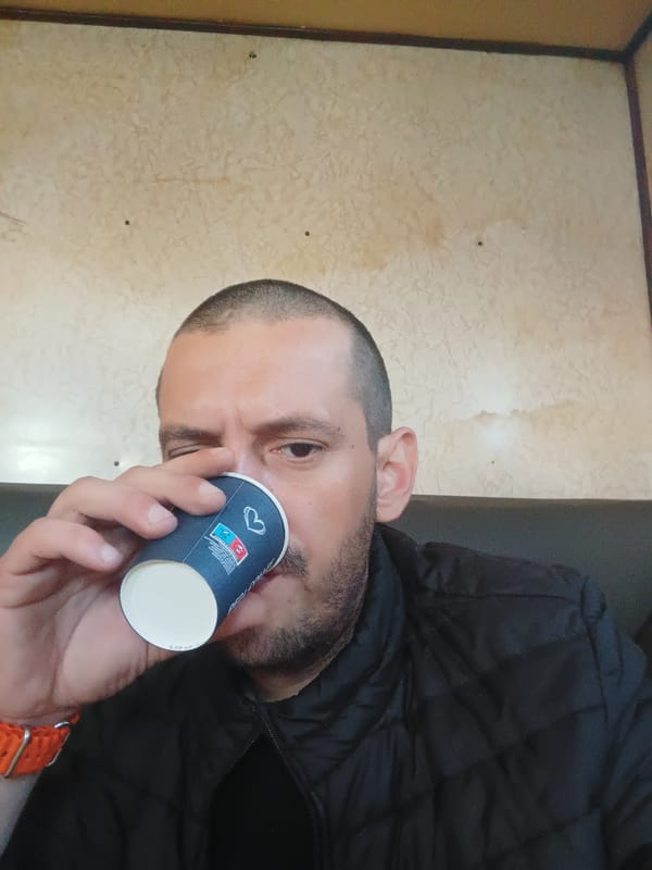 Man in black jacket drinks from cup near patterned wall
