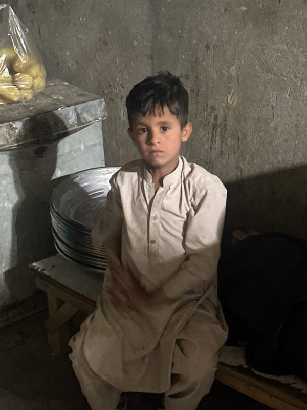 Boy sits with metal plates in Quetta interior setting