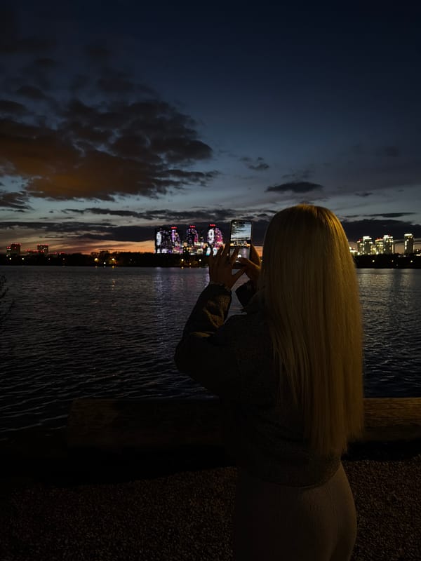 Woman photographs illuminated Kazan Family Center at night