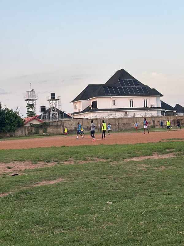 Football session on a dusty Abuja field, late afternoon.