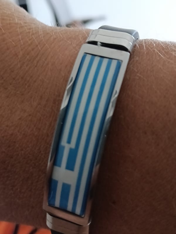 Greek flag bracelet and a portable speaker on a wooden floor