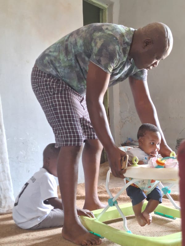 Man holds baby in walker in Nigerian residential area