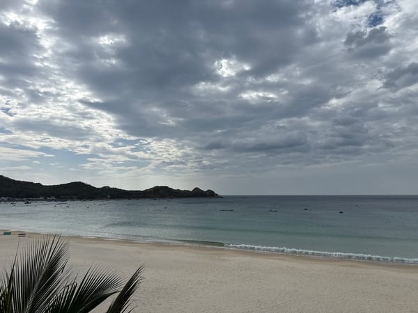 Quiet tropical beach under cloudy skies, calm water throughout