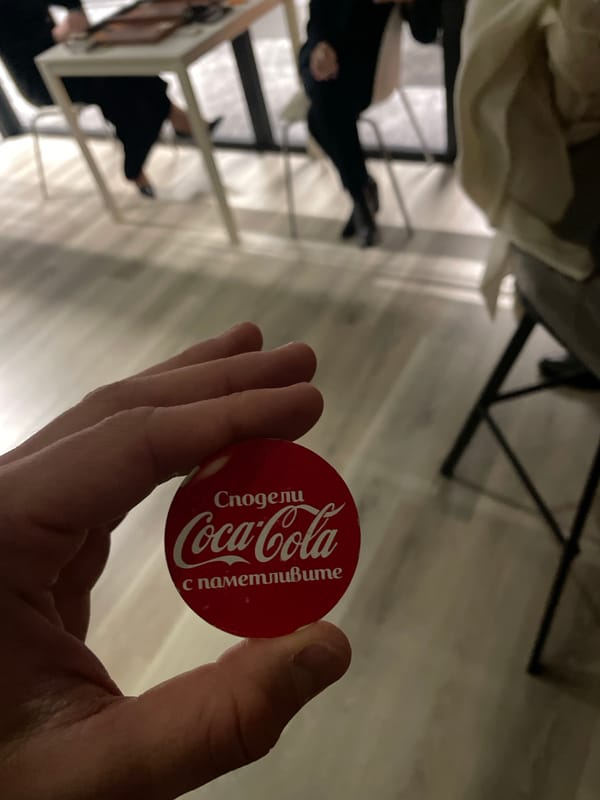 Person holds Coca-Cola promotional button with Cyrillic text in Sofia