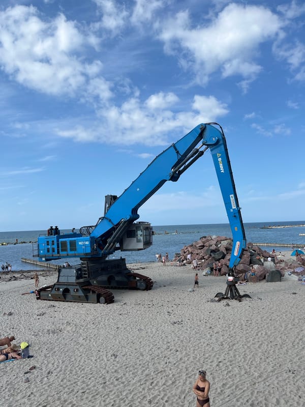 Excavator on Baltic beach near a fenced pink building, Svetlogorsk