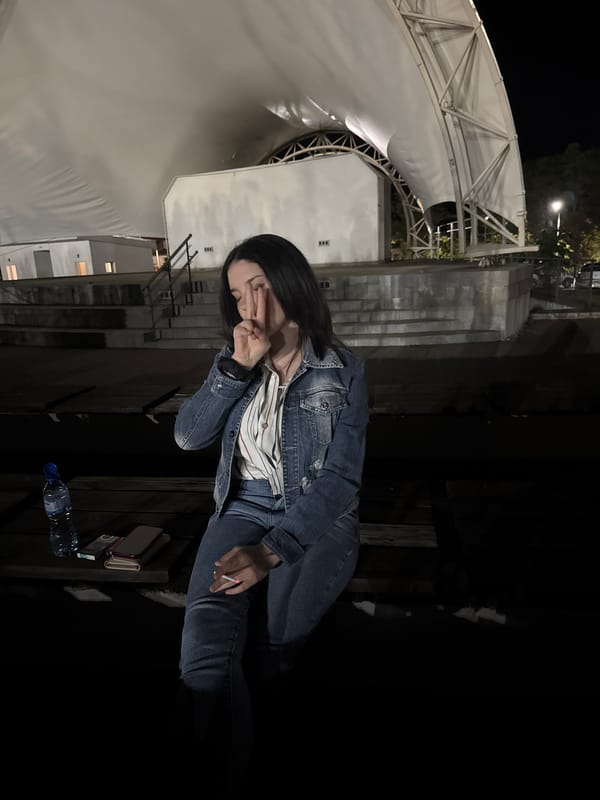 Woman sits alone smoking cigarette on bench at night