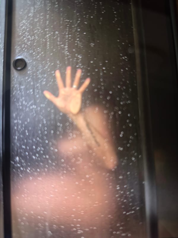 Figure observed behind wet glass surface, hand pressed against barrier