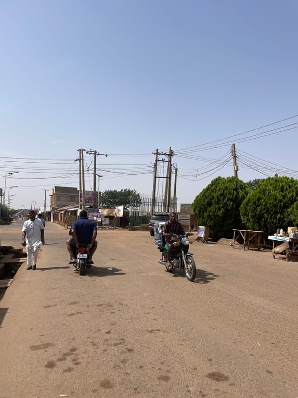 Two motorcyclists travel along paved street in Jos, Nigeria