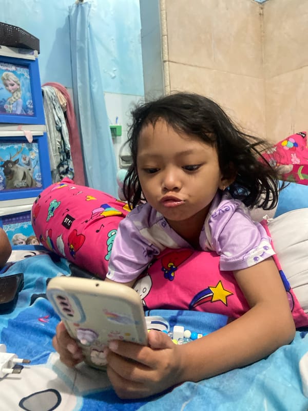 Child uses smartphone on bed in Gelam, Indonesia