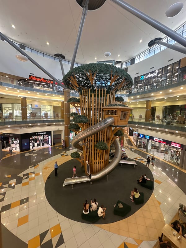 Shopping mall atrium with a treehouse play structure and quirky signage