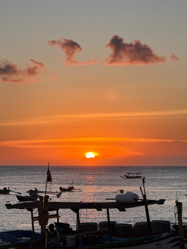 Airplane crosses sun during Kuta sunset with boats below