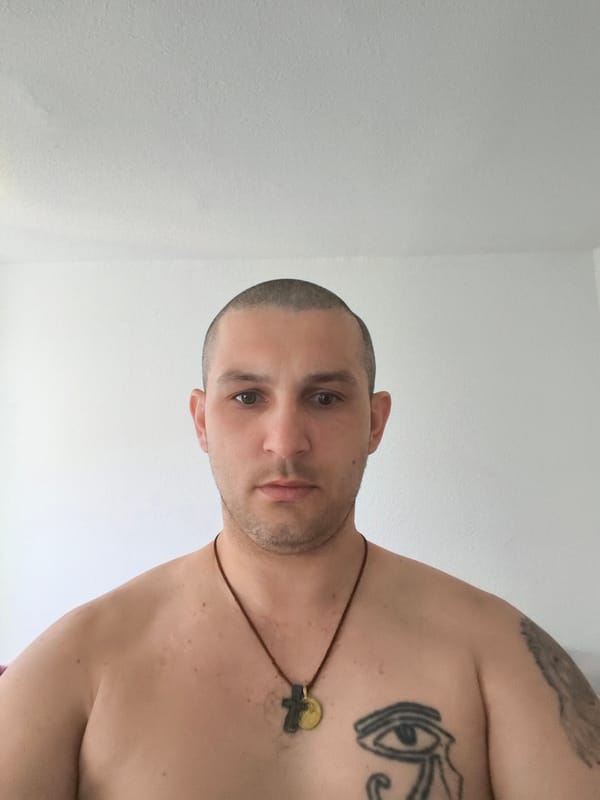 Indoor portrait session: shirtless, tattooed, cord necklace.