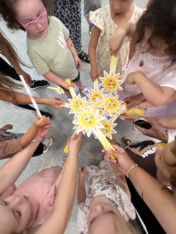 Kids and adults celebrate with handmade sun decorations indoors in Kiryat Bialik