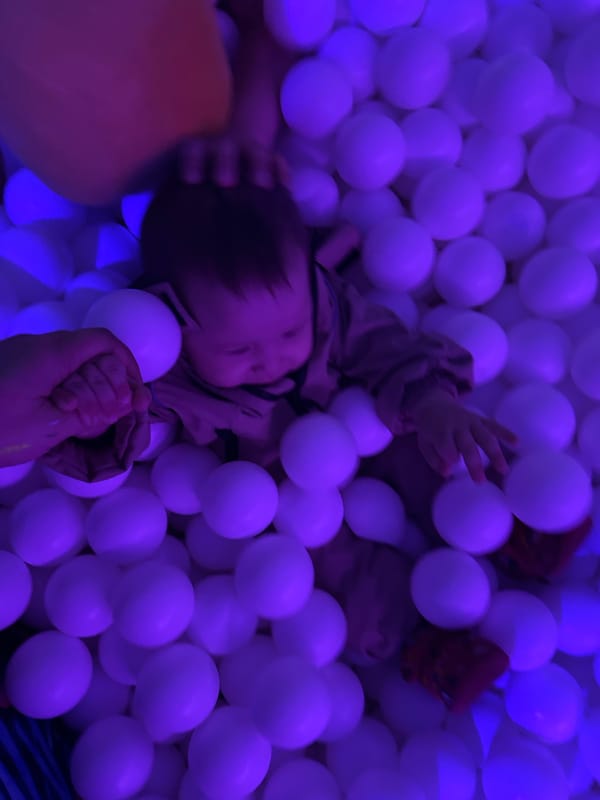 Children play in purple-lit ball pit at indoor facility