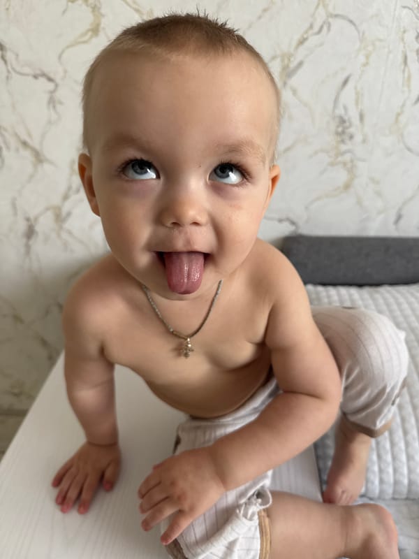 Baby with cross necklace observed resting on white surface