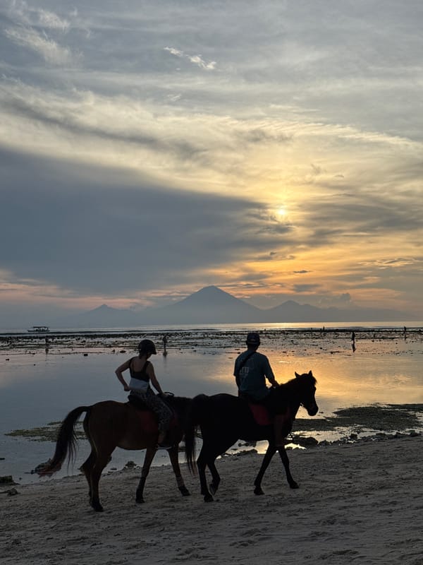 Two horseback riders captured on Indonesian beach at sunset