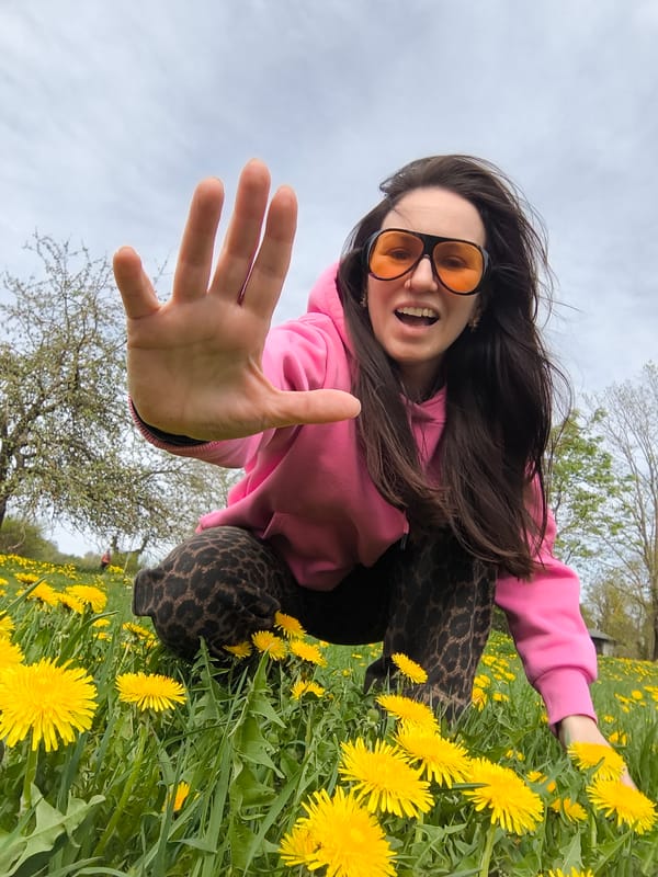 Woman in pink hoodie poses in Riga dandelion field