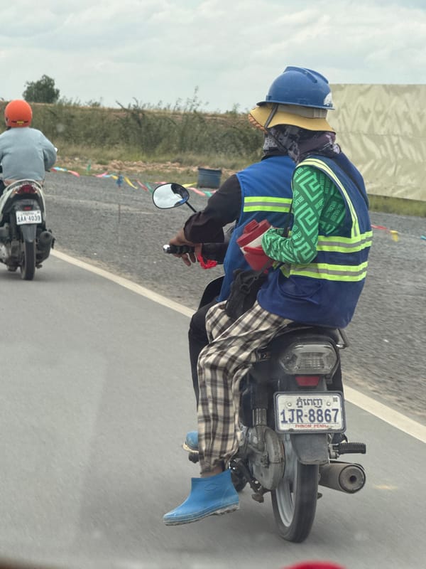Motorcycle riders navigate Krong Ta Khmau streets, layered up against the elements