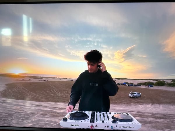 DJ performs with controller in sandy outdoor setting at sunset