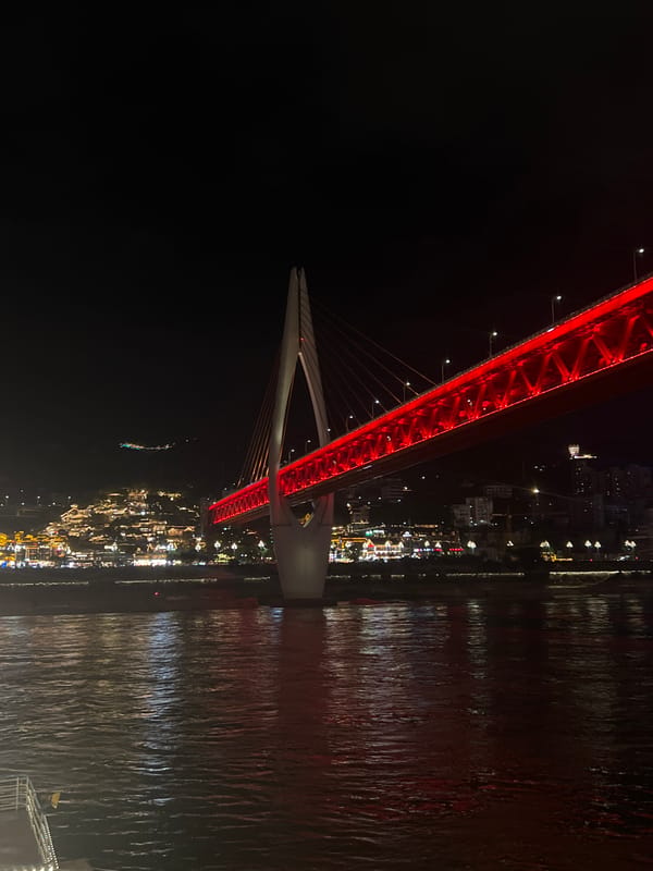 Chongqing's red-lit Hongyadong Bridge at night, cruise ship passing beneath