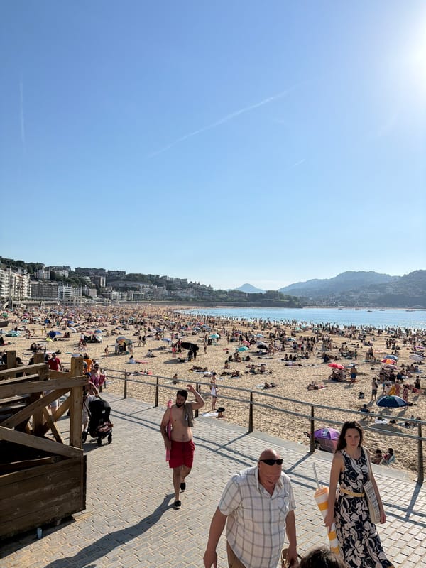 Crowded San Sebastián beach features sand art on sunny afternoon