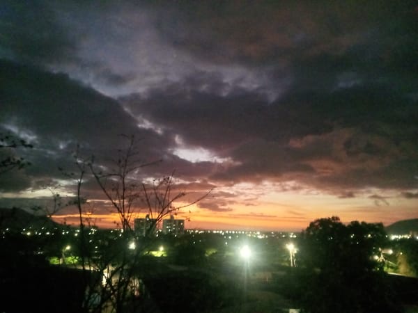 Urban sunset creates orange purple sky through dark clouds