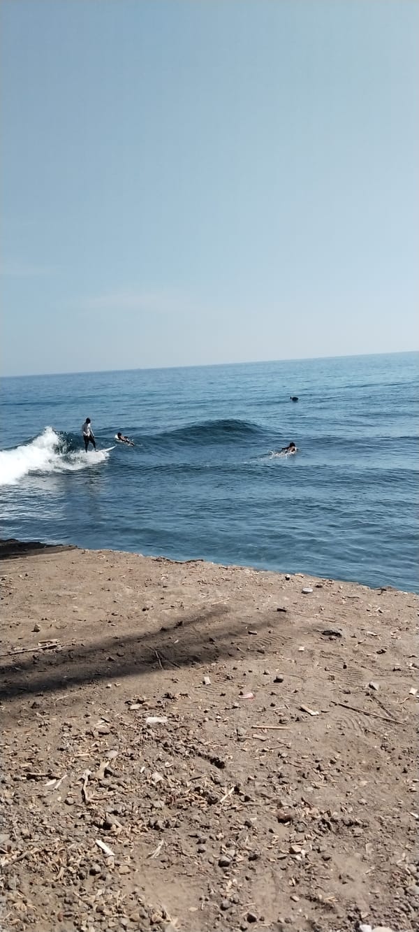 Surfers in the water off Senggigi's rocky coastline