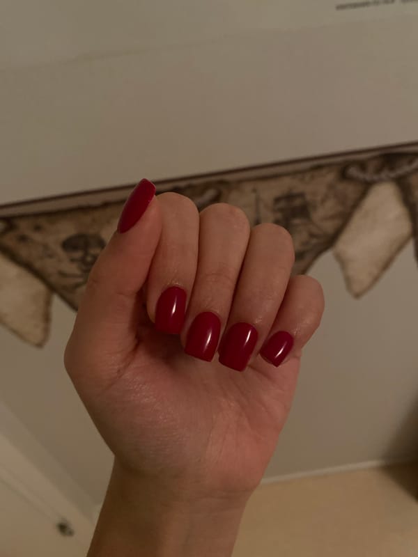 Red square nails photographed against pirate-themed wall art
