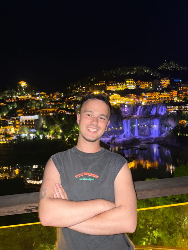 Tourist poses on balcony overlooking illuminated Furong Ancient Town