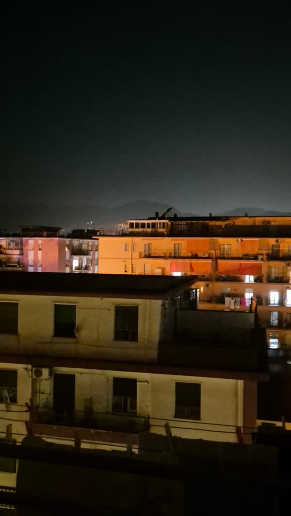 City apartment blocks lit up at night, hills in the distance