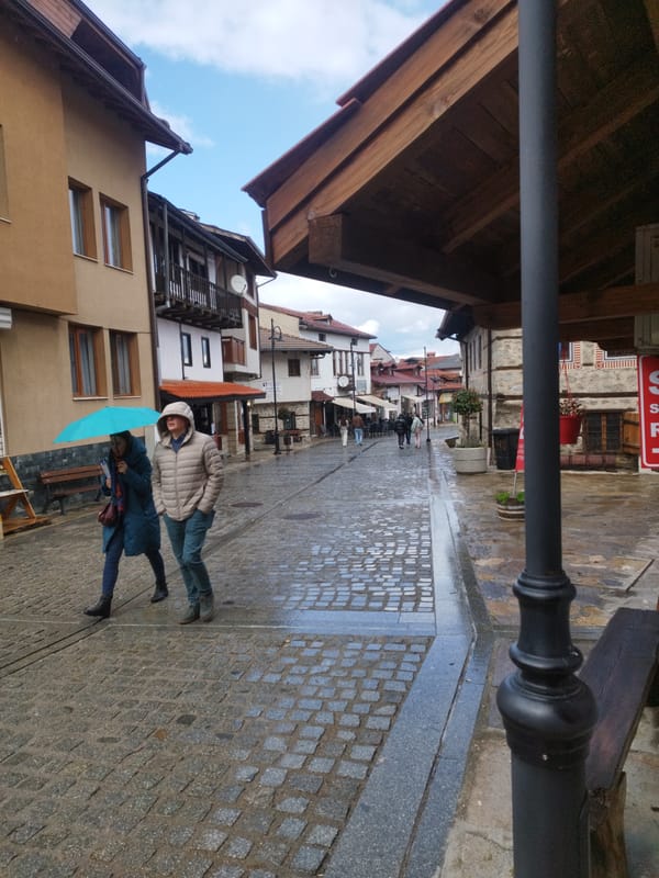 Pedestrians with umbrella navigate wet cobblestone street in Bansko