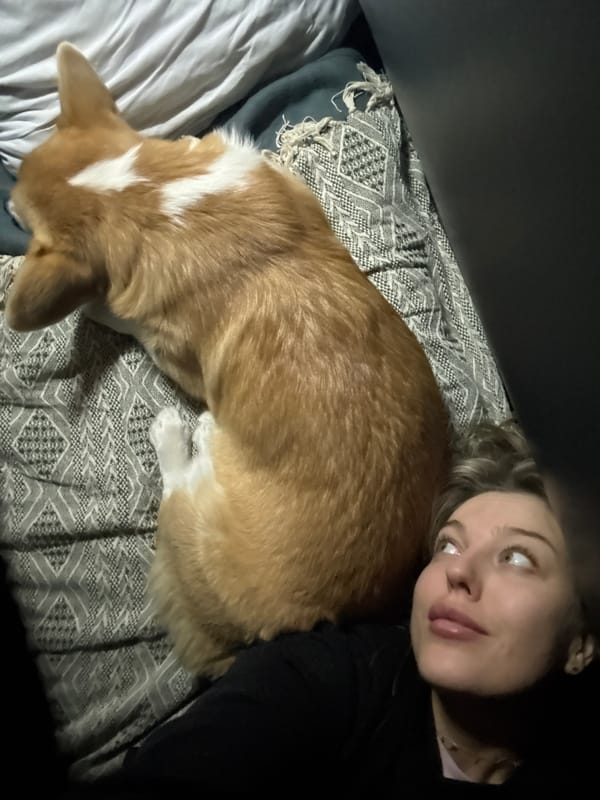 Woman rests with corgi on bed in Russia
