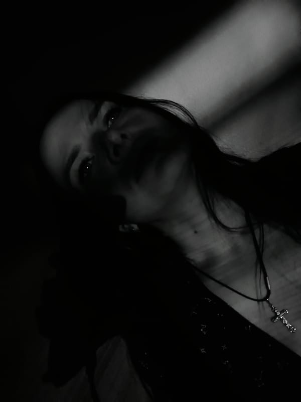 Person photographed in dramatic lighting wearing cross pendant