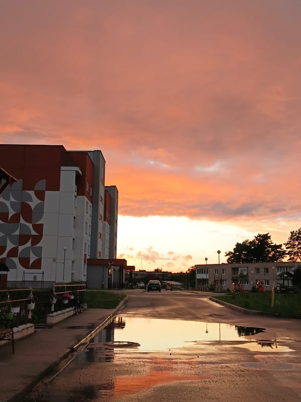 Post-rain puddles mirror a vivid sunset in rural Belarus