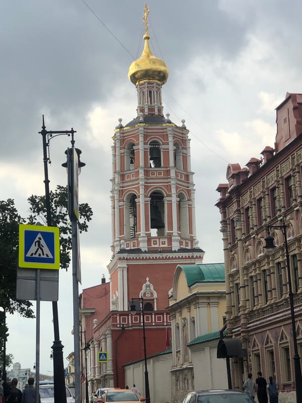 Bell tower and cafe life on a cloudy Cyrillic-script city street