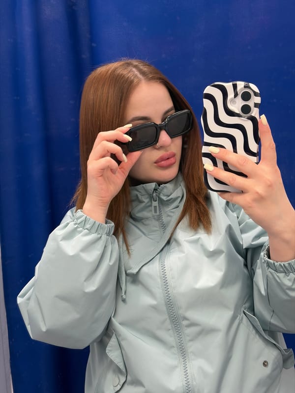 Woman in blue jacket takes outdoor selfies, adjusts sunglasses