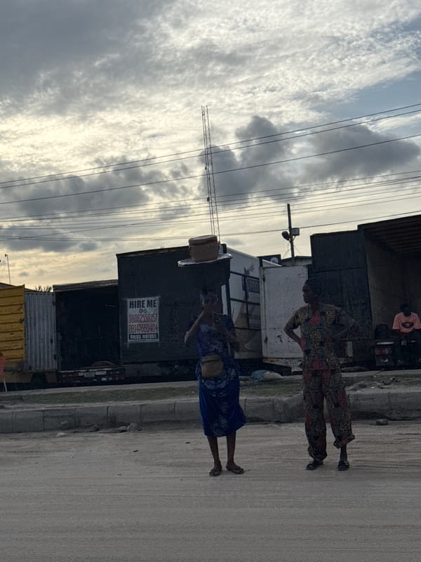 Two women walk roadside in Lagos, one carrying box