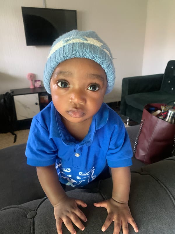 Small child in blue beanie plays around a home in Nigeria