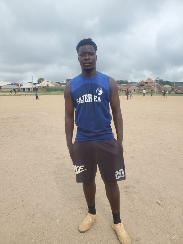 Standing on a dirt field in a 'SAJEH FA' sleeveless shirt