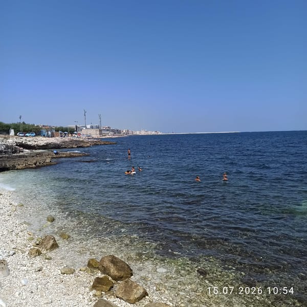 Sunny morning at Molfetta's rocky shore, people in and out of the water