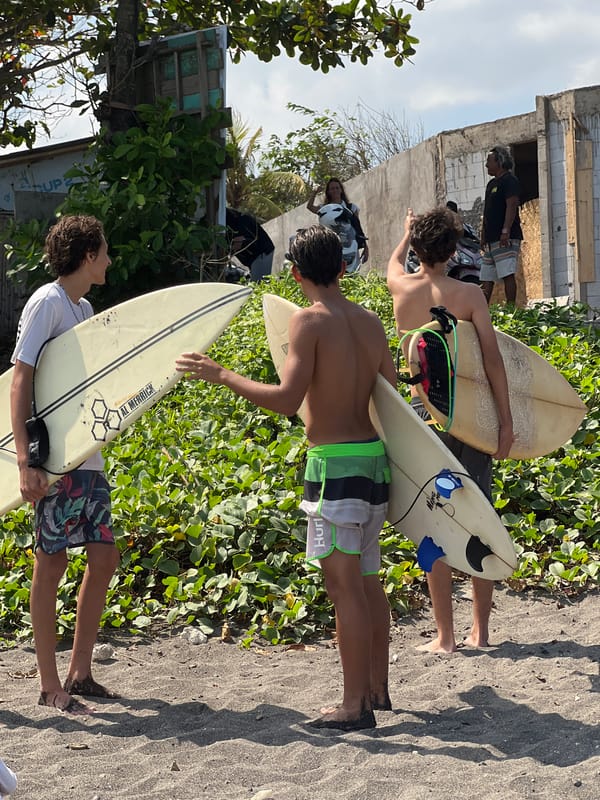 Surfers and beachgoers on Mengwi's volcanic sand coast