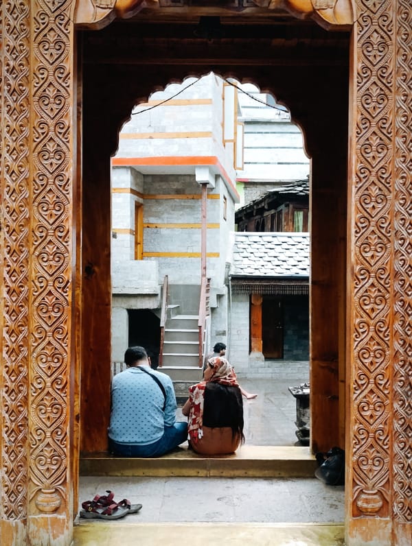 Sitting on temple steps beneath carved wooden archways in Vashisht