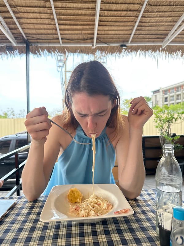 Woman documents pasta meal at outdoor restaurant in Thailand