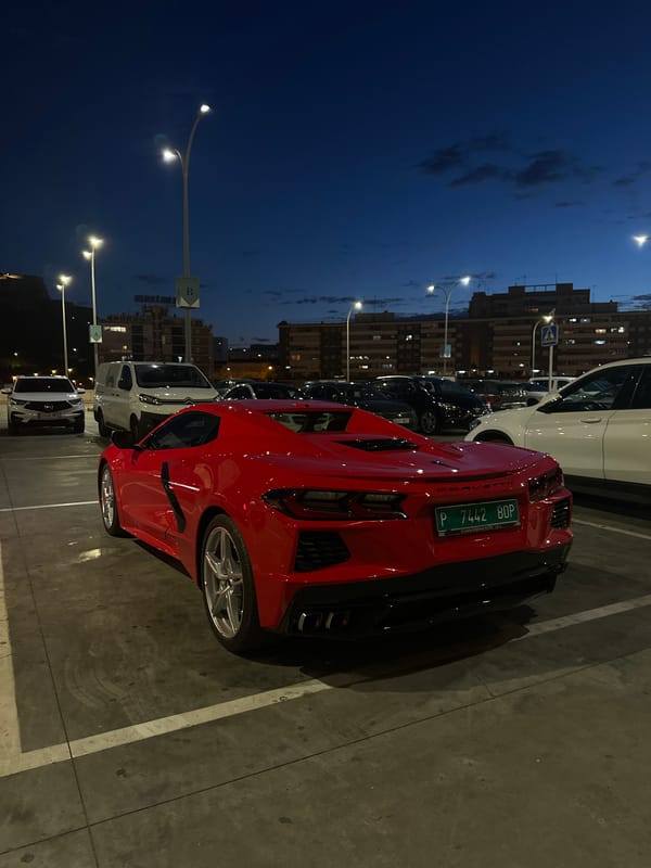 Girl walks through parking lot near red Corvette at night