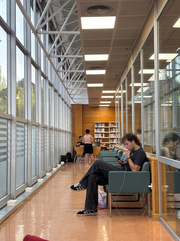 Downtime in a Las Rozas library, phone out, red shades clipped