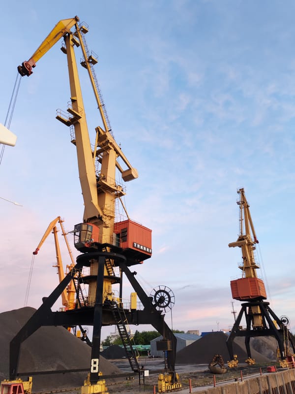 Cruise ship passes a crane-lined port at dusk